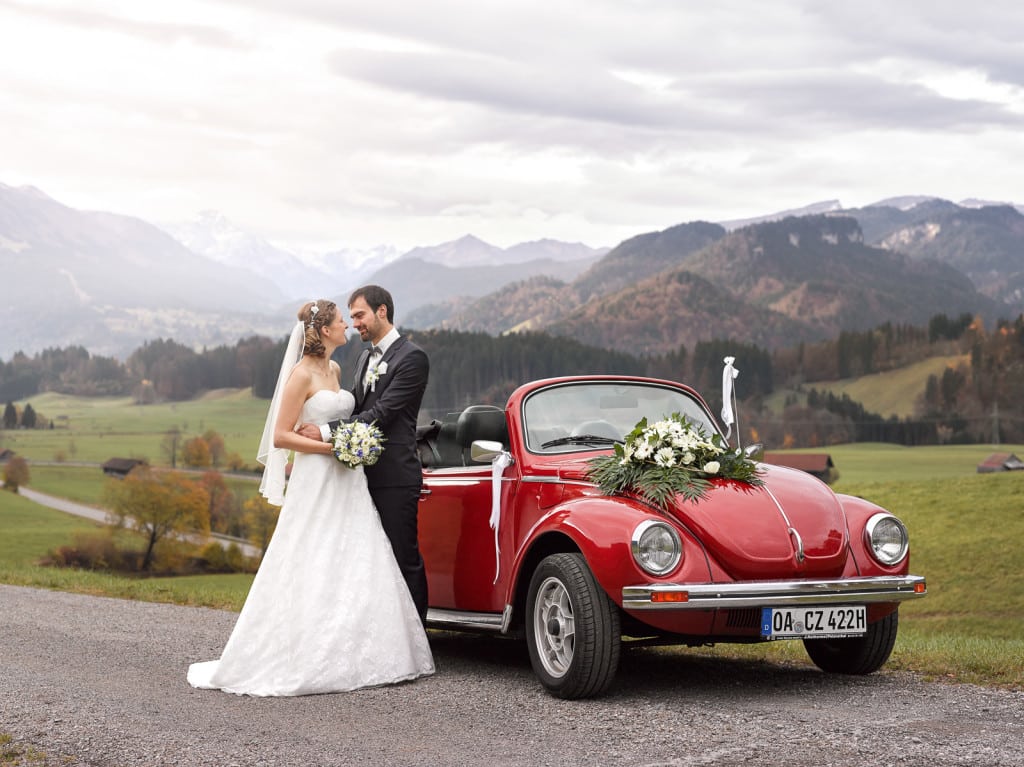 Brautpaar mit VW Käfer Oldtimer vor auf einem Hügel mit den Alpen im Hintergrund | Hochzeitsfotograf im Allgäu